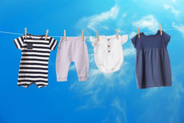 Mavi gökyüzüne karşı çamaşır ipinde kurumuş farklı bebek kıyafetleri.