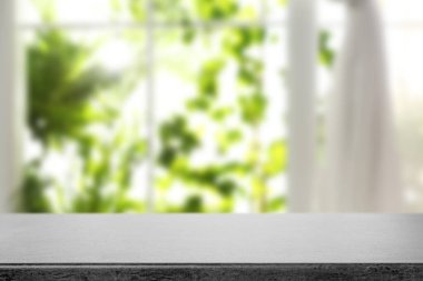 Boş taş masa, pencereye karşı, odada perde var.