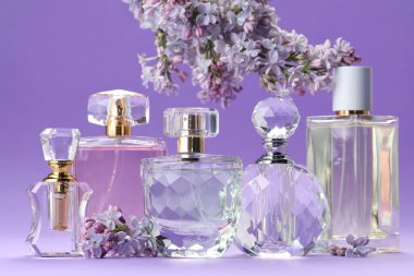 Parfümlü şişeler ve mor arkaplanda leylak çiçekleri, yakın plan.