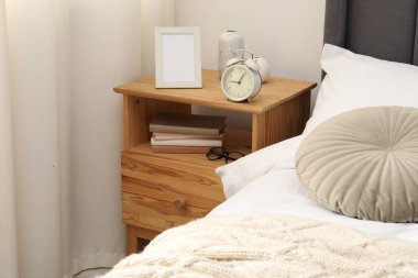 Yatağın yanında alarm saati ve dekorasyonu olan komodinin yanında.