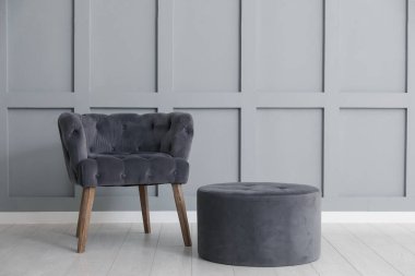 Açık gri duvarın yanında rahat koltuk ve puf. Kapalı mekanda, metin için boşluk.