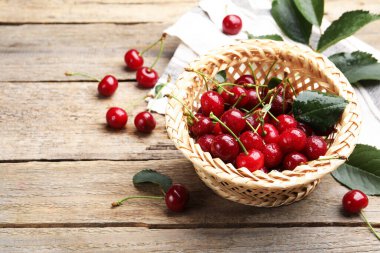 Taze ıslak kirazlar, yapraklar ve hasır sepet ahşap masada, yakın plan.