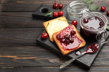 Lezzetli kiraz reçelli tostlar ve siyah ahşap masada taze meyveler, yakın plan. Metin için boşluk