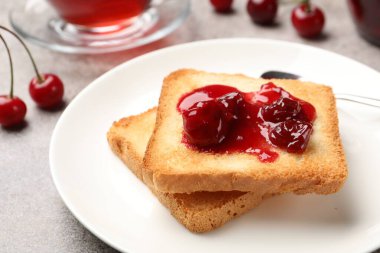 Lezzetli kiraz reçelli tostlar, çay ve taze meyveler gri masada, yakın plan.