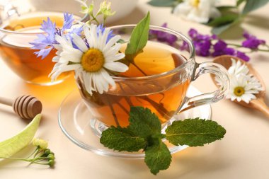 Cam fincanlarda aromatik bitki çayı, farklı çiçekler ve bej arka planda nane şekeri, yakın plan.
