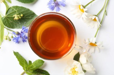 Cam fincanda aromatik bitki çayı, farklı çiçekler ve beyaz arka planda nane şekeri.