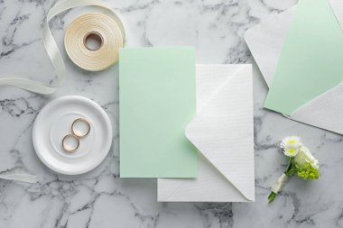 Düğün davetiyesi, altın yüzükler, kurdele ve zarf beyaz mermer masa, düz uzanma