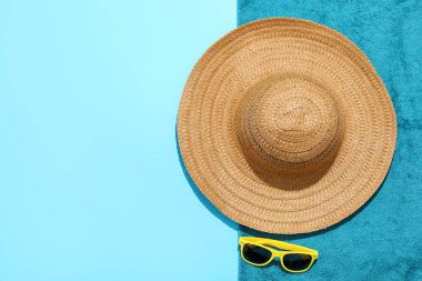 Hasır şapka, güneş gözlüğü ve açık mavi arka planda plaj havlusu, üst manzara. Metin için boşluk