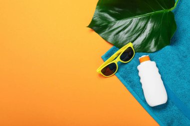 Plaj havlusu, güneş gözlüğü, güneş kremi ve turuncu arka planda yaprak. Metin için boşluk