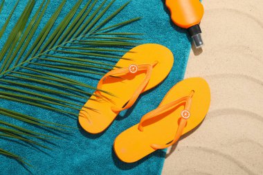 Plaj havlusu, parmak arası terlik, güneş kremi ve açık havada palmiye yaprağı.