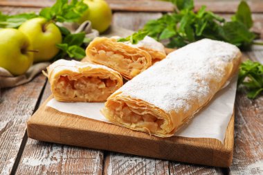 Ahşap masada pudra şekeri, nane ve meyveli elmalı turtalar, yakın plan.