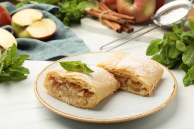 Lezzetli elmalı turta parçaları pudra şekeri, nane, meyve ve tarçın beyaz mermer masada, yakın plan.