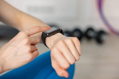 Kadın spor salonunda spor yaparken takip cihazını kontrol ediyor, yakın plan. Metin için boşluk