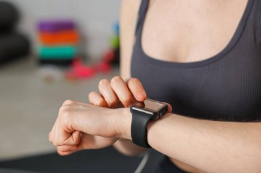 Kadın spor salonunda spor yaparken takip cihazını kontrol ediyor, yakın plan.