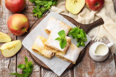 Lezzetli elmalı turta parçaları pudra şekeri, nane ve ahşap masa üzerinde meyve, düz uzanmış