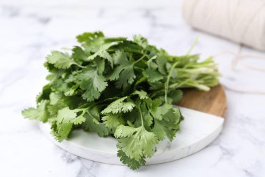 Taze aromatik kişniş, beyaz mermer masa üzerindeki kesme tahtası ve iplik, yakın plan.