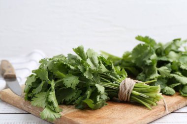 Beyaz ahşap masada taze kişniş ve bıçakla tahta kesme, yakın plan. Metin için boşluk