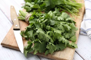 Tahta kesme tahtası taze kişniş ve bıçak beyaz ahşap masada, yakın plan.