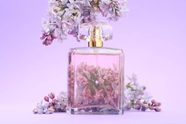 Parfüm şişesi ve mor arkaplanda leylak çiçekleri, yakın plan.