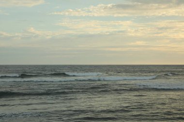 Gün batımında bulutlu gökyüzünün altında güzel dalgalı bir deniz.