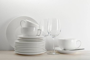 Beyaz duvarın yanındaki açık ahşap masada farklı temiz bulaşık takımı.