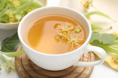 Fincanda taze ıhlamur çayı ve beyaz masada çiçekler, yakın plan.