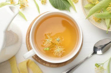 Fincanda taze ıhlamur çayı ve beyaz ahşap masada çiçekler.