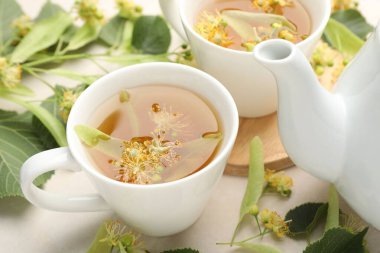 Taze ıhlamur çayı, çaydanlık ve çiçekler beyaz masada, yakın plan.