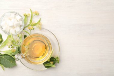 Taze ıhlamur çayı, şeker küpleri ve beyaz ahşap masa üzerinde çiçekler, düz uzanma. Metin için boşluk