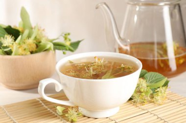 Taze ıhlamur çayı, çaydanlık ve çiçekler beyaz masada, yakın plan.