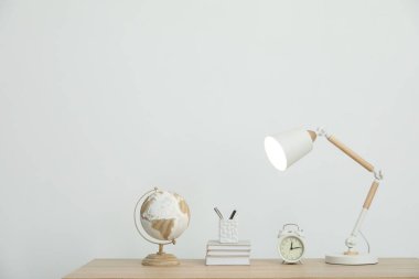 Lamba, kitaplar, kırtasiye, çalar saat ve küre beyaz duvarın yanındaki ahşap masada.