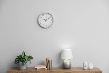 Lamba, kitaplar, vazolar ve yeşil bitkiler beyaz duvarın yanındaki ahşap masada.