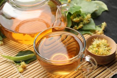 Lezzetli ıhlamur çayı, çaydanlık, yapraklar ve çiçekler koyu masada, yakın plan.