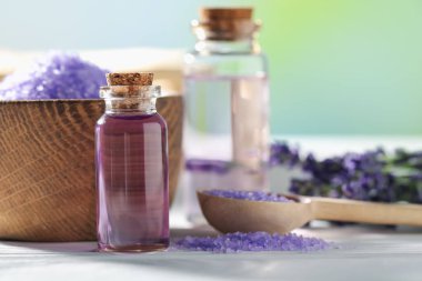 Beyaz ahşap masa üzerinde lavanta yağı, deniz tuzu ve çiçekler, yakın plan.