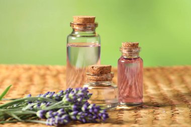 Hasır masanın üzerinde lavanta yağı ve çiçek şişeleri, yakın plan.