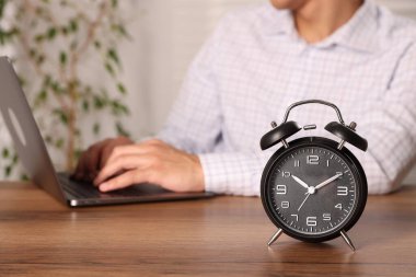 Son teslim tarihi. Çalar saat ve adam tahta masada dizüstü bilgisayarda çalışıyor, seçici odaklanma