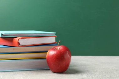 Farklı kitaplar ve gri masada kırmızı elma tahtaya karşı, yakın plan. Metin için boşluk