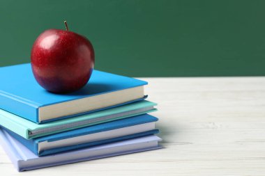 Tahtaya karşı beyaz tahta üzerinde farklı defterler ve kırmızı elma, yakın plan. Metin için boşluk