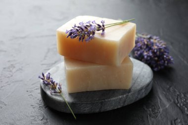 Aromatik sabun barları ve lavanta çiçekleri koyu dokulu masa üzerinde, yakın plan.