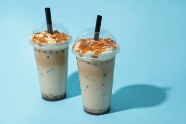 Açık mavi zemin üzerinde plastik bardaklarda lezzetli süt köpüğü çayı