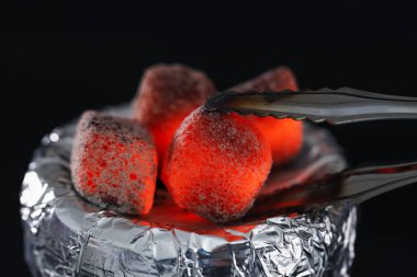 Siyah arka planda folyoyla kaplanmış nargile tutacağının üzerine yanan kömür küpü koymak, yakın plan