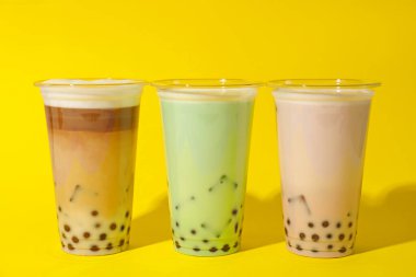 Sarı arka planda plastik bardakta lezzetli süt köpüğü çayı.