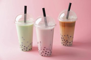 Pembe arka planda plastik bardakta lezzetli sütlü çay.