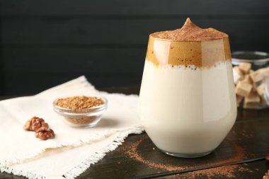 Bardakta lezzetli dalgona kahvesi, granüller, ceviz ve kahverengi şeker ahşap masada, yakın plan.