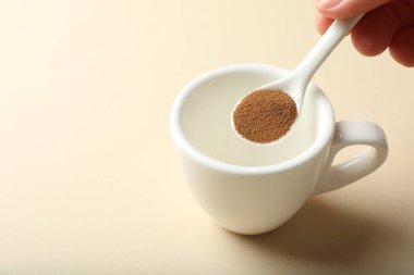 Bej arka planda hazır kahveyi fincana koyan kadın, yakın plan. Metin için boşluk