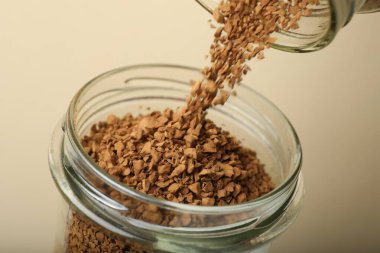 Bej arka planda kavanoza hazır kahve dolduruluyor, yakın plan.