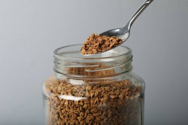 Gri arka planda kaşıkla hazır kahve içmek, yakın plan.