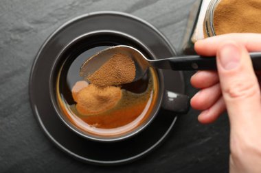 Siyah masada hazır kahveyi fincana koyan kadın.