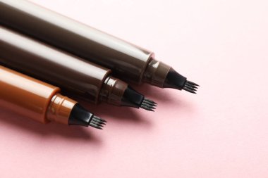 Açık pembe arka planda sıvı kaş kalemleri, yakın plan.