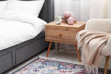 Yatağın yanında alarm saati ve dekorasyonu olan komodinin yanında.
